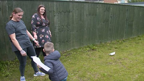 A little boy throwing a paper plane as his mums look on.