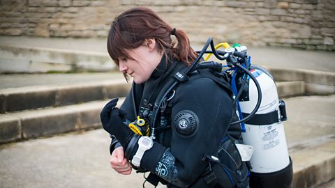 Marie putting on her scuba gear with an oxygen tank on her back.