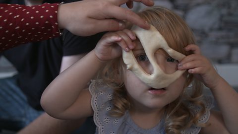 Girl looking through holes in playdough. 