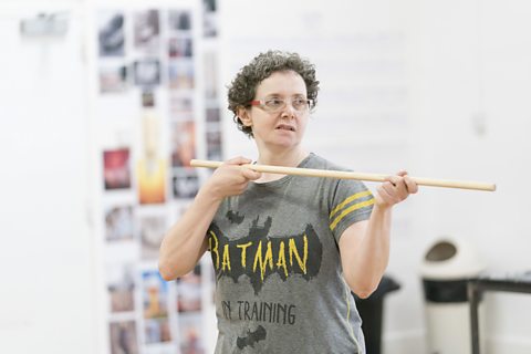 An actress rehearses with a wooden pole prop