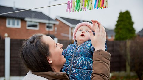 A mum and a baby looking at pegs on a washing line.