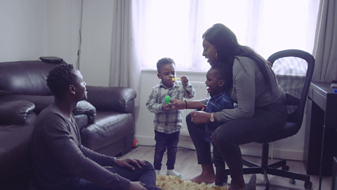 Dad sat on floor and mum on chair while their children play with bubbles