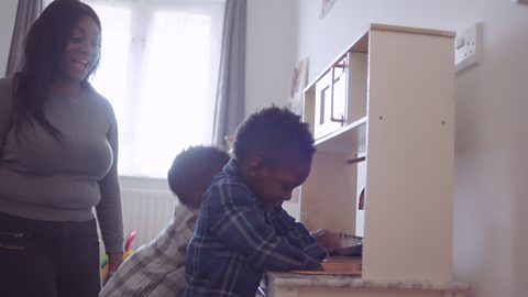 Mum looking on as her toddlers play with toy kitchen.