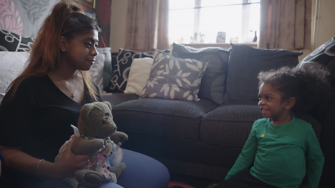 Mum holding teddy and talking to her young child.