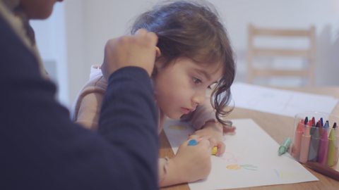 A little girl drawing as her mum moves her hair from her face.