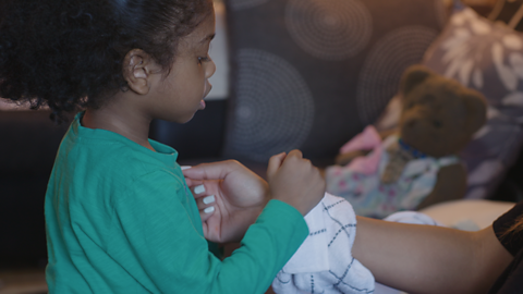 A little girl wrapping a tea towel around her mum's wrist.