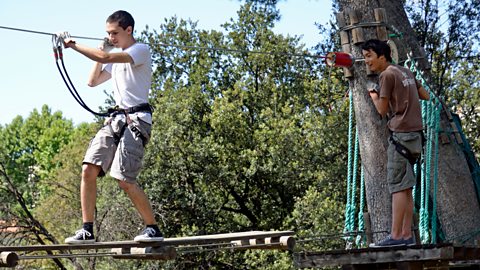 Teenage boys (16-17) on suspended footbridge in an adventure park.