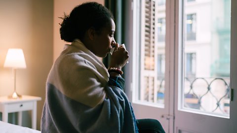 woman sat drinking a cup of tea and looking out of the window