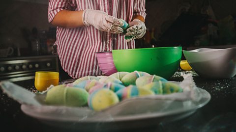 A person wearing latex gloves moulding bath bombs in a kitchen.