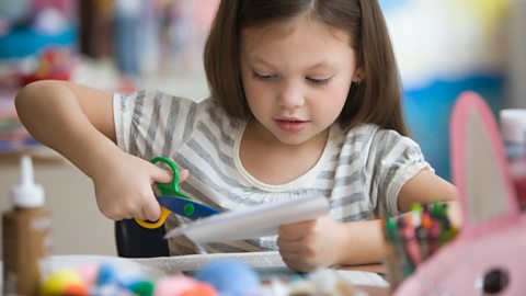 A young girl cutting up a magazine to make a collage