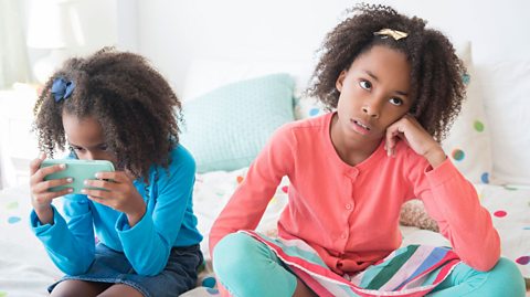 Two sisters: one looking bored and the other on a phone