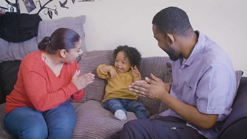 Mum, dad and toddler sat on sofa clapping