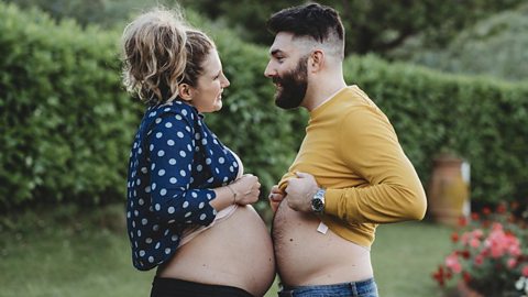 A young pregnant woman presses her baby bump against a young man's belly.