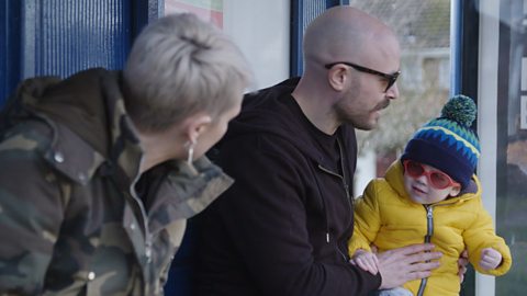 Mum and dad talking to little boy outdoors. 