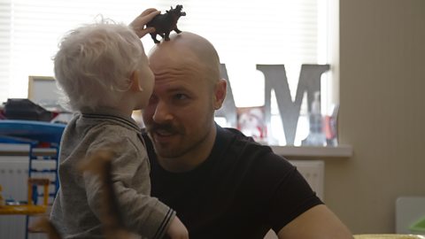 Milo putting a dinosaur toy on his dad's head.