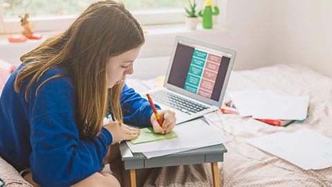 Girl studies in her room on her own using a pen and sticky notes