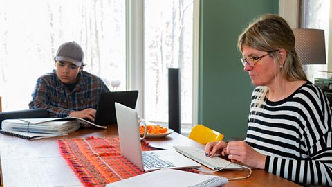 Mum showing her son how working from home is done as they share a desk and concentrate on their own work