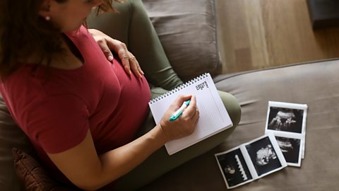 Pregnant woman sitting on the sofa writing a list of baby names