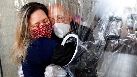 EPA A woman hugs her 82-year-old father through a "hug curtain", in Sao Paulo, Brazil, one of the worst affected regions in the world (Credit: EPA)