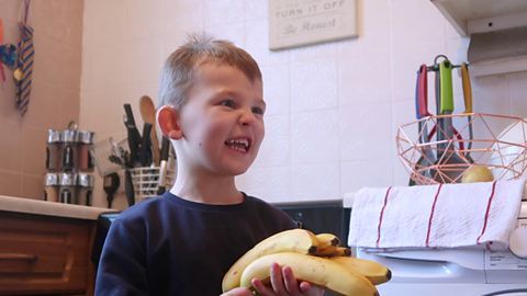 A little boy holding a bunch of bananas.