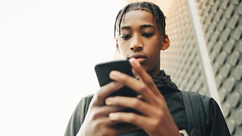 A boy with dreadlocks looking at a mobile phone in his hands.