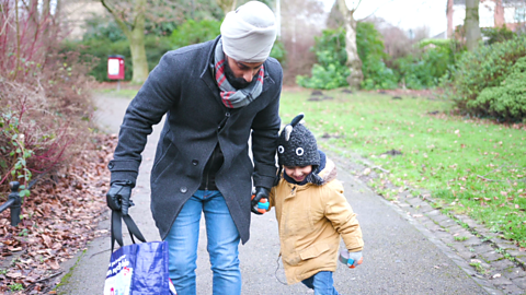 Dad holding hand of toddler as they walk through park.