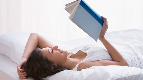 Girl laying on a white bed reading a blue book.