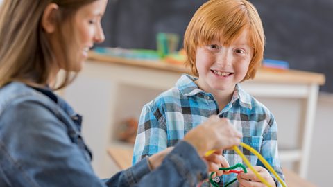 Young boy and his mum play with coloured pipe cleaners.