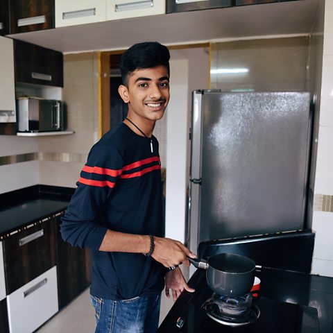 A boy cooking using a pan on a stove