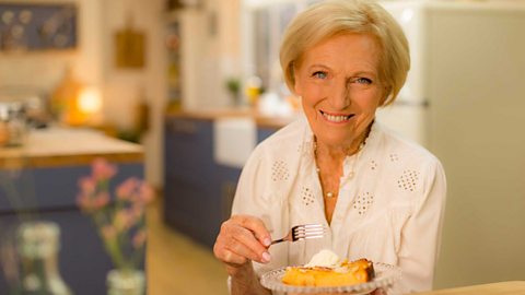 Mary Berry stands with a slice of pie. 