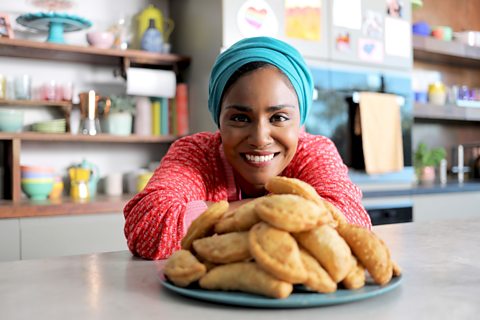 Nadiya Hussain sits smiling with a plate of pecan pies