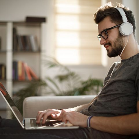 A young man with headphones on, typing.