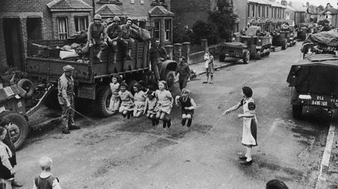 A US soldier helps turn the skipping rope as children play jump rope in the street.