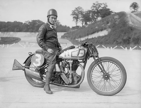 Miss Beatrice Shilling sits astride her Norton motorcycle