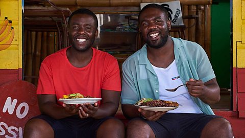 Craig and Shaun McAnuff sit outside a brightly painted cafe with a plate of food each 