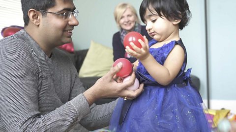 A little girl is playing with a couple of balls with her dad 