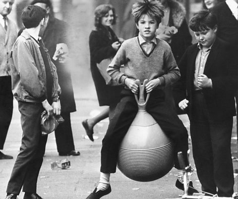 A boy playing on a space hopper in the street.