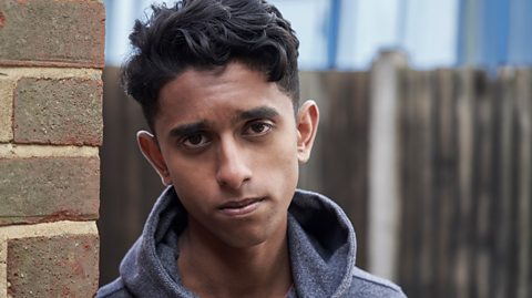 Teenage boy looking anxious as he leans against a brick wall 