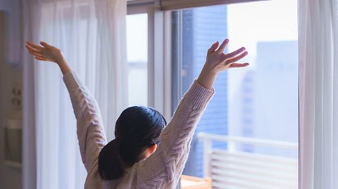 Someone stretching their arms and looking out the window at a glorious morning