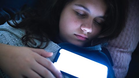 A girl asleep in bed with the glow of her phone shining onto her face