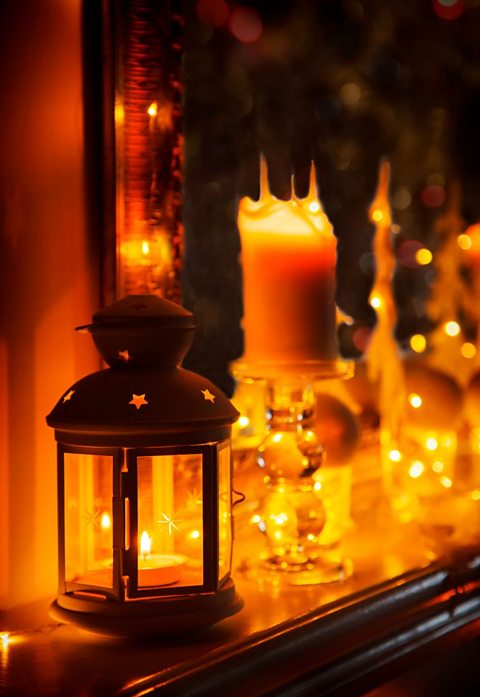 Christmas Lights Decor on Fireplace, including a lit tea light inside of a star patterned lantern.