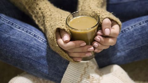 A girl holds a glass of coffee with milk in her hands