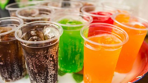 plastic disposable glasses filled with different types of brightly coloured fizzy drinks 