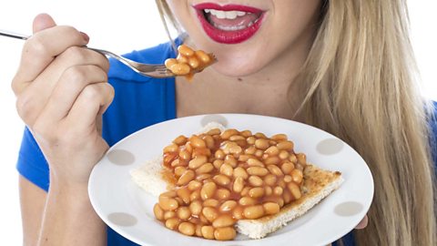 A woman eats a plate of beans on toast