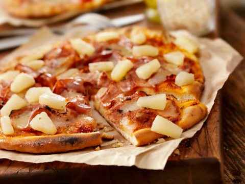 A thin crust ham and pineapple pizza, served on greaseproof paper on top of a wooden board.