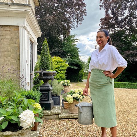 Paula standing by the flowers on her porch with a watering can.