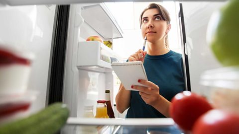 New year, new.... fridge? How to improve your fridge organisation so you waste less food and spark more joy in the kitchen… A woman looks through her fridge with a pen and pad