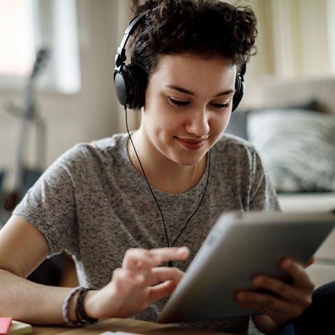 A young person with headphones on, using a tablet.