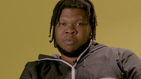 Kadeem Ramsay wearing a grey hoody standing in front of a mustard background.