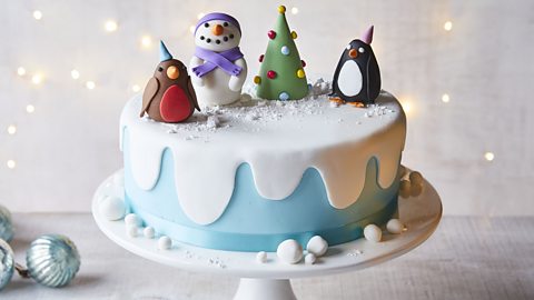 A decorated Christmas cake with a robin, snowman, penguin and Christmas tree figures on top